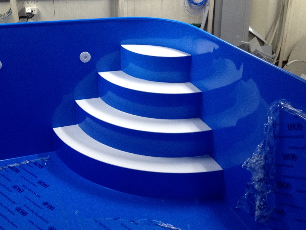 Zaoblený modrý bazén s bielymi nášľapmi a modrou lemovou rúrkou
