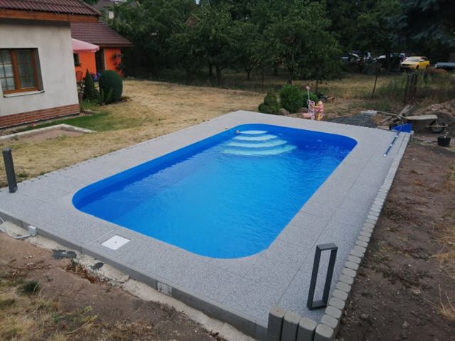 Zaoblený modrý bazén s bílými nášlapy