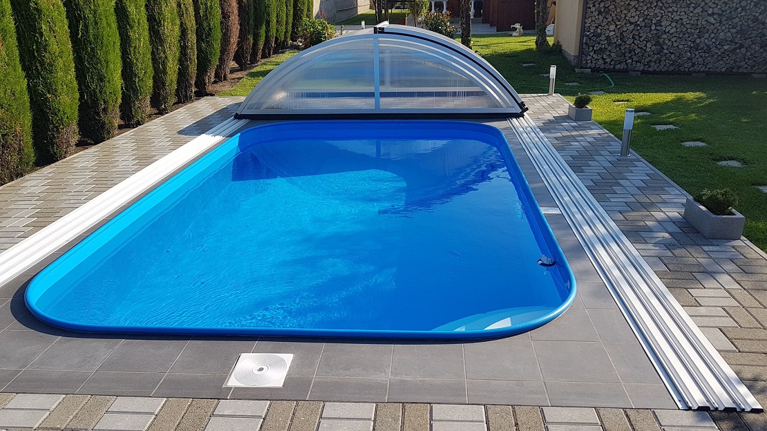 Zaoblený modrý bazén s bílými nášlapy a lemovou trubkou